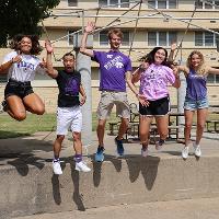 Five college students jumping off of a short wall.