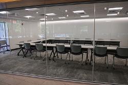 An outside view of a glass-walled classroom with movable tables and chairs.