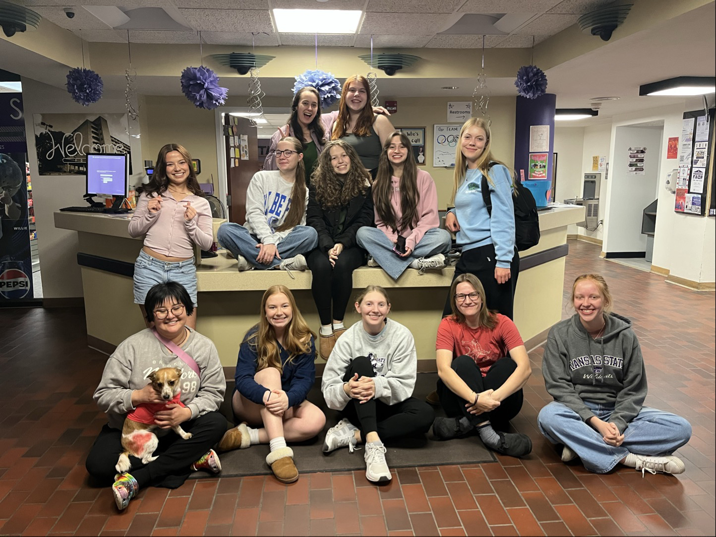 A group of women sitting on and around the front desk of a residence hall