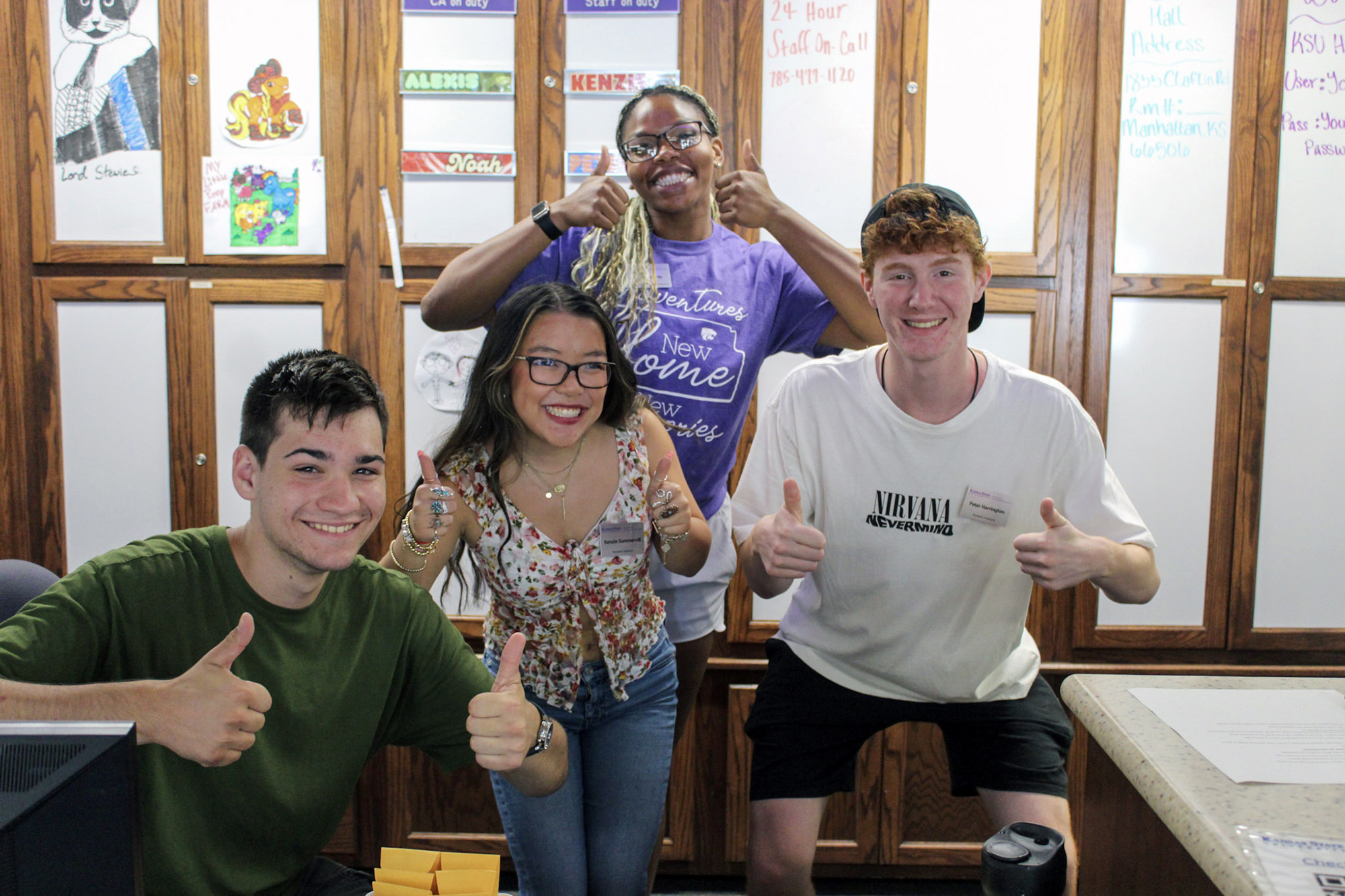 A group of student workers smiling and posing behind a residence hall front desk