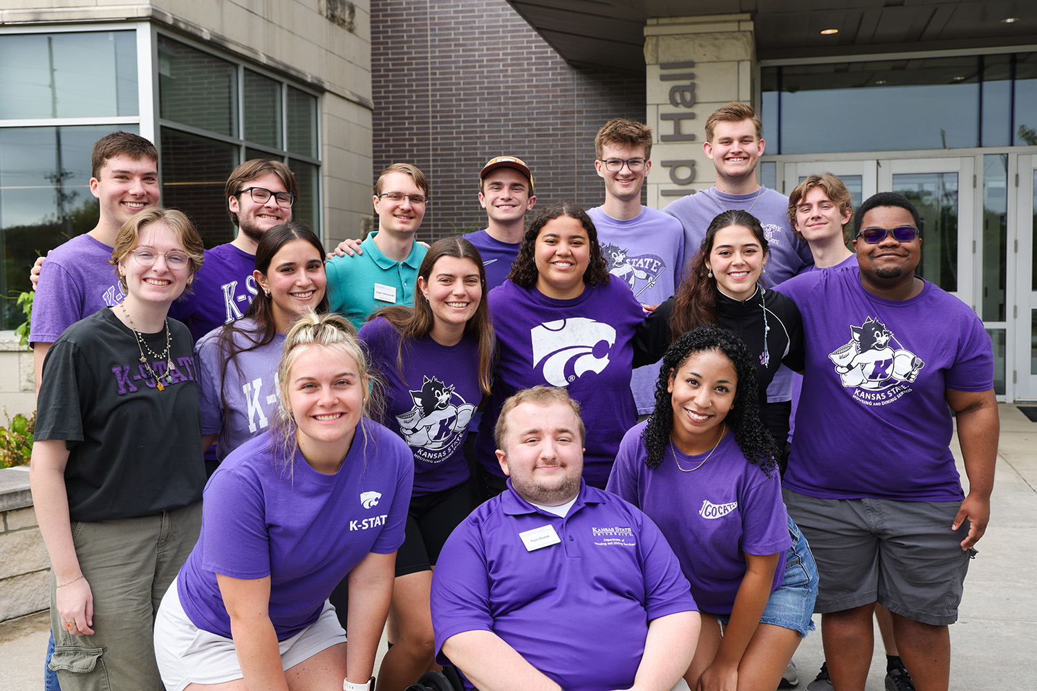 A group of K-State students standing in front of the entrance of Wefald Hall.
